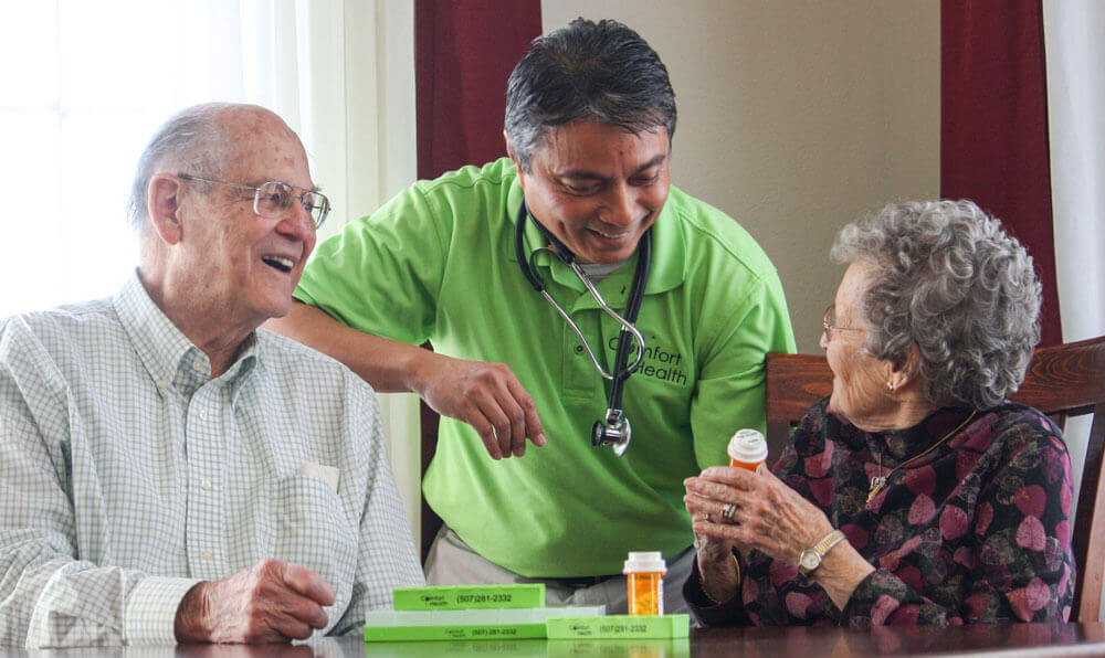 smiling older couple with aide and medication