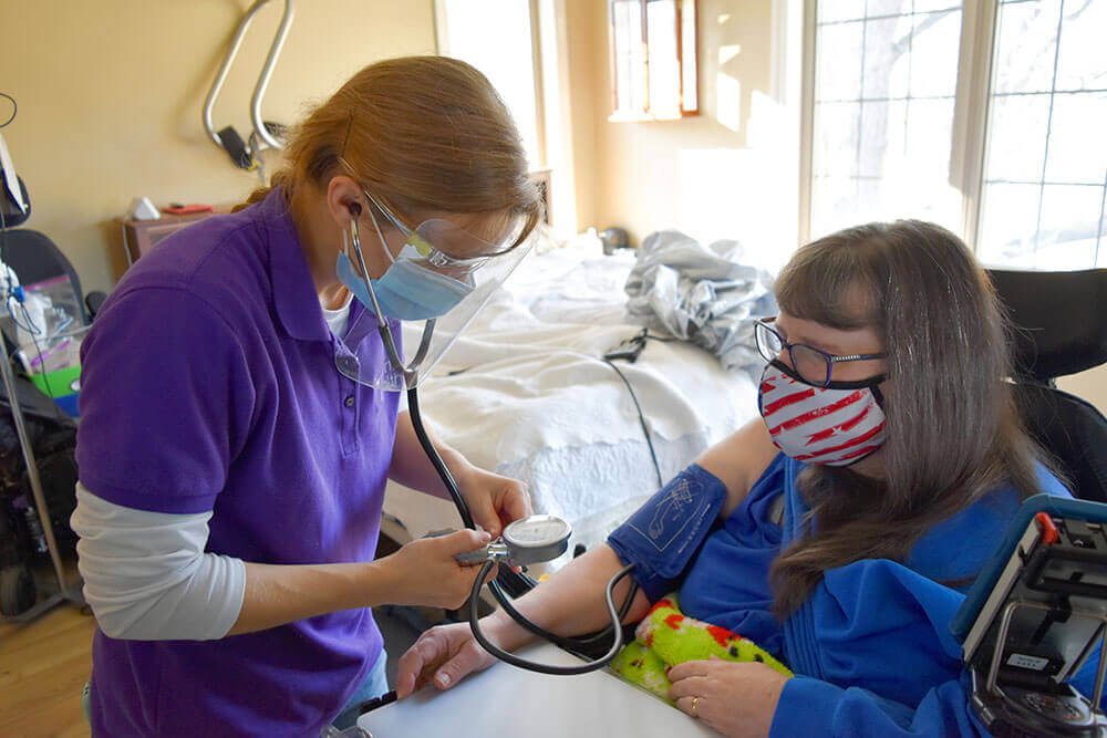 masked woman taking patient's blood pressure