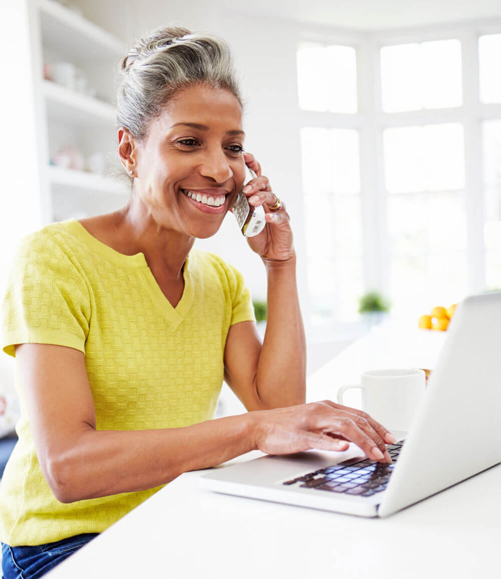 smiling older woman talking on the phone in front of a laptop